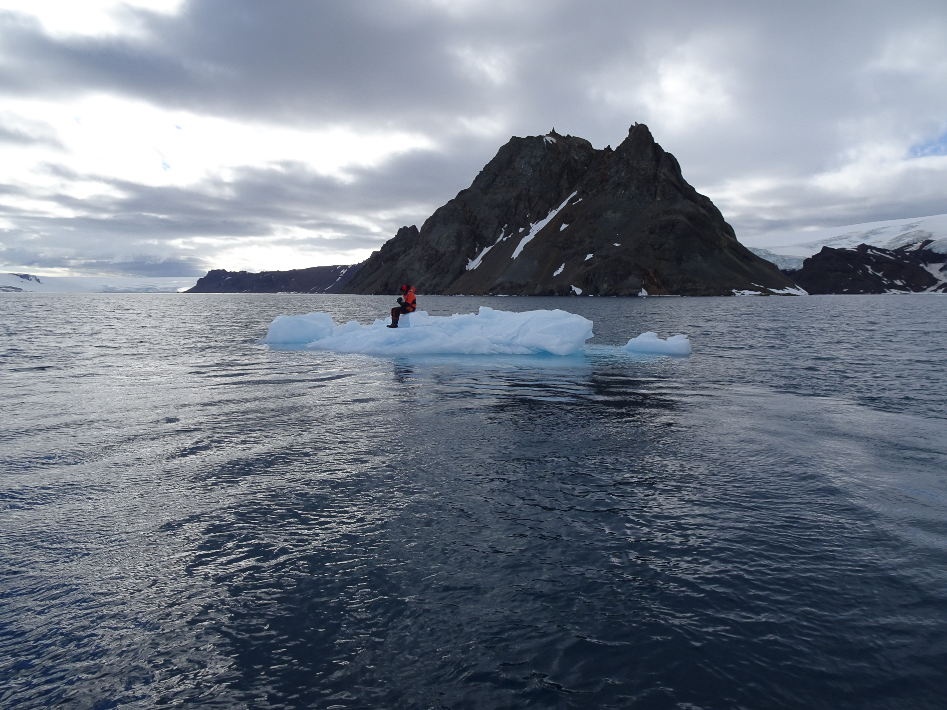 Na zdjęciu mężczyzna siedzący na krze lodowej znajdującej się na wodzie. Za nim wzgórze oraz niebo. Autor Tomasz Kurczaba
