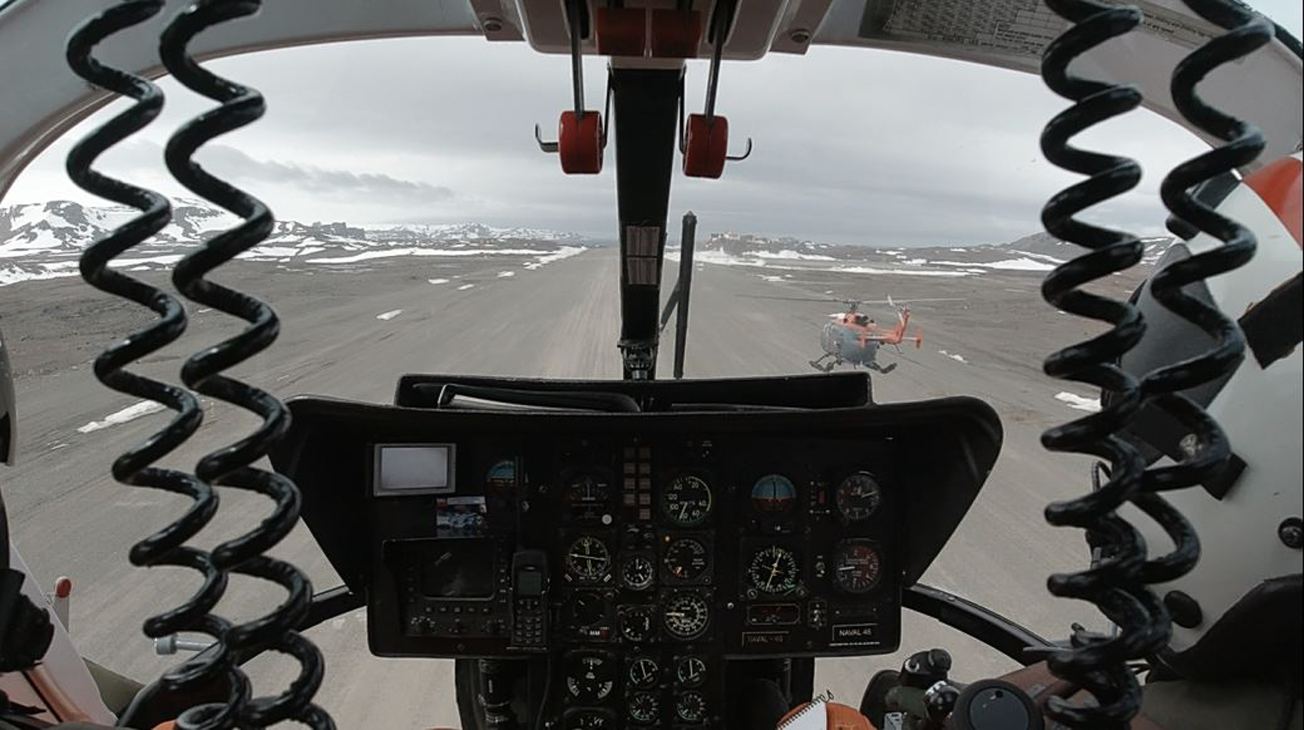 Na zdjęciu widok z kabiny pilota z kokpitem. Przed -helikopter, po lewej i prawej stronie ziemia i wzgórza pokryte śniegiem. Autor Tomasz Kurczaba 