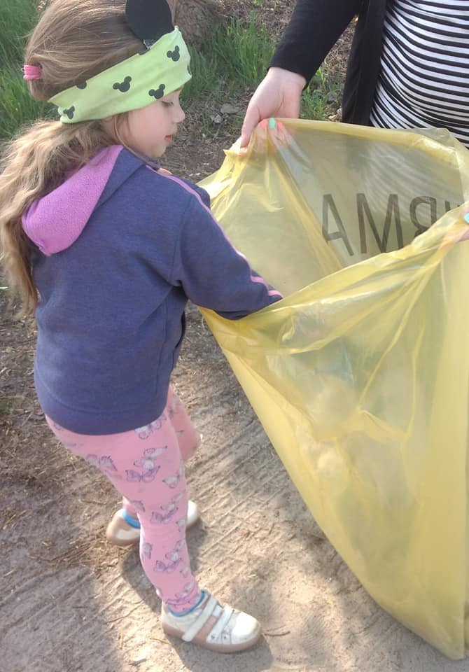Na zdjęciu dziewczynka wrzucająca śmieci do żółtego worka, który trzyma rodzic.
