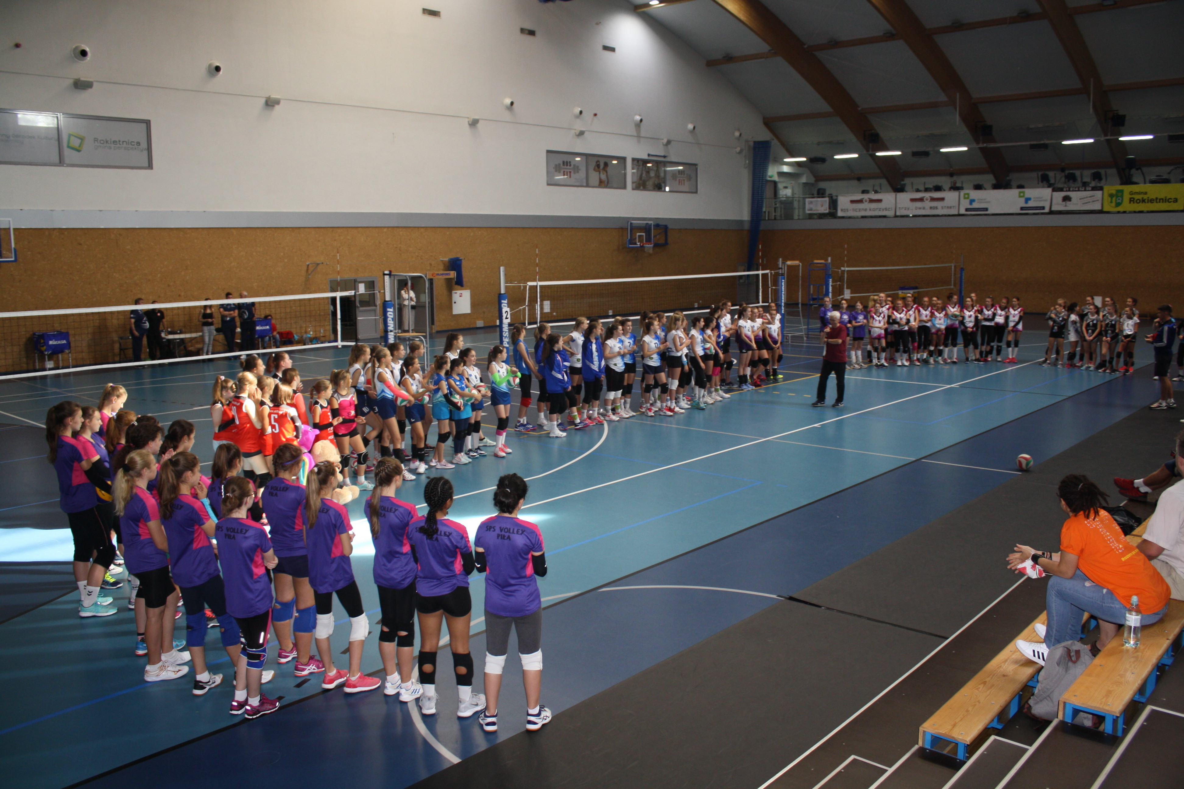 Na zdjęciu zawodniczki Lider Cup - turnieju siatkówki dziewcząt stojące w półokręgu. Na środku pan Piotr Paupa - prezes UKS Lider.