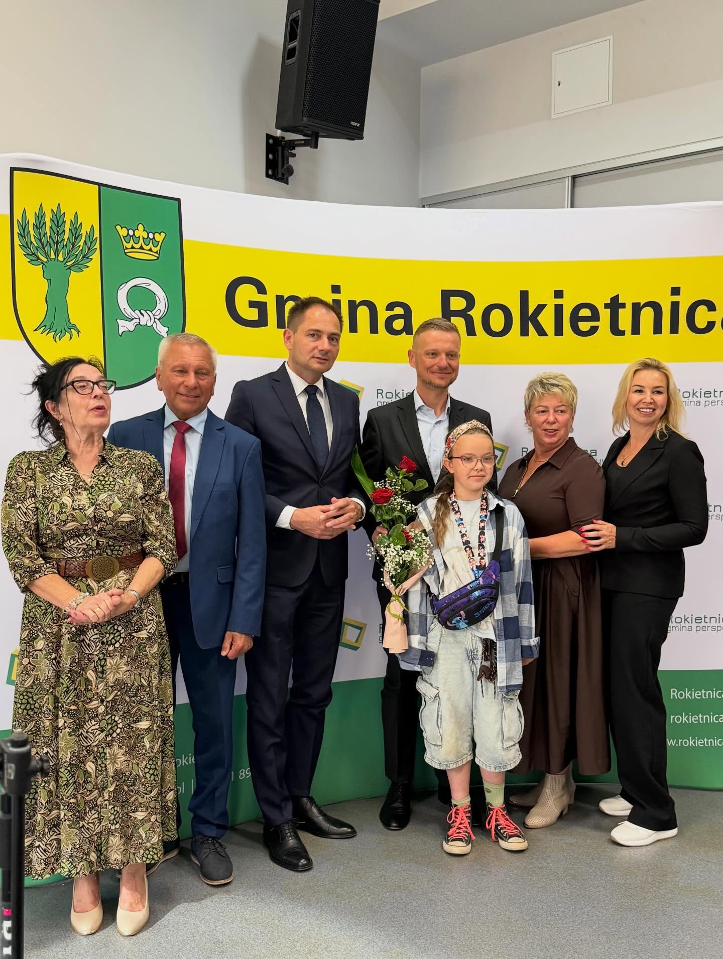 Ścianka Gminy Rokietnica, W&oacute;jt Gminy Rokietnica, Przewodnicząca Rady Gminy Rokietnica, Dyrektorka Gminnego Ośrodka Kultury w&nbsp;Rokietnicy i&nbsp;laureaci wraz z&nbsp;statuetkami, dyplomami i&nbsp;kwiatami. 