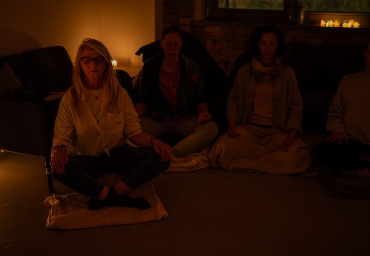 Zdjęcie: 3 kobiety siedzące niedaleko siebie po turecku w&nbsp;p&oacute;łmroku. Za nimi świeczki.