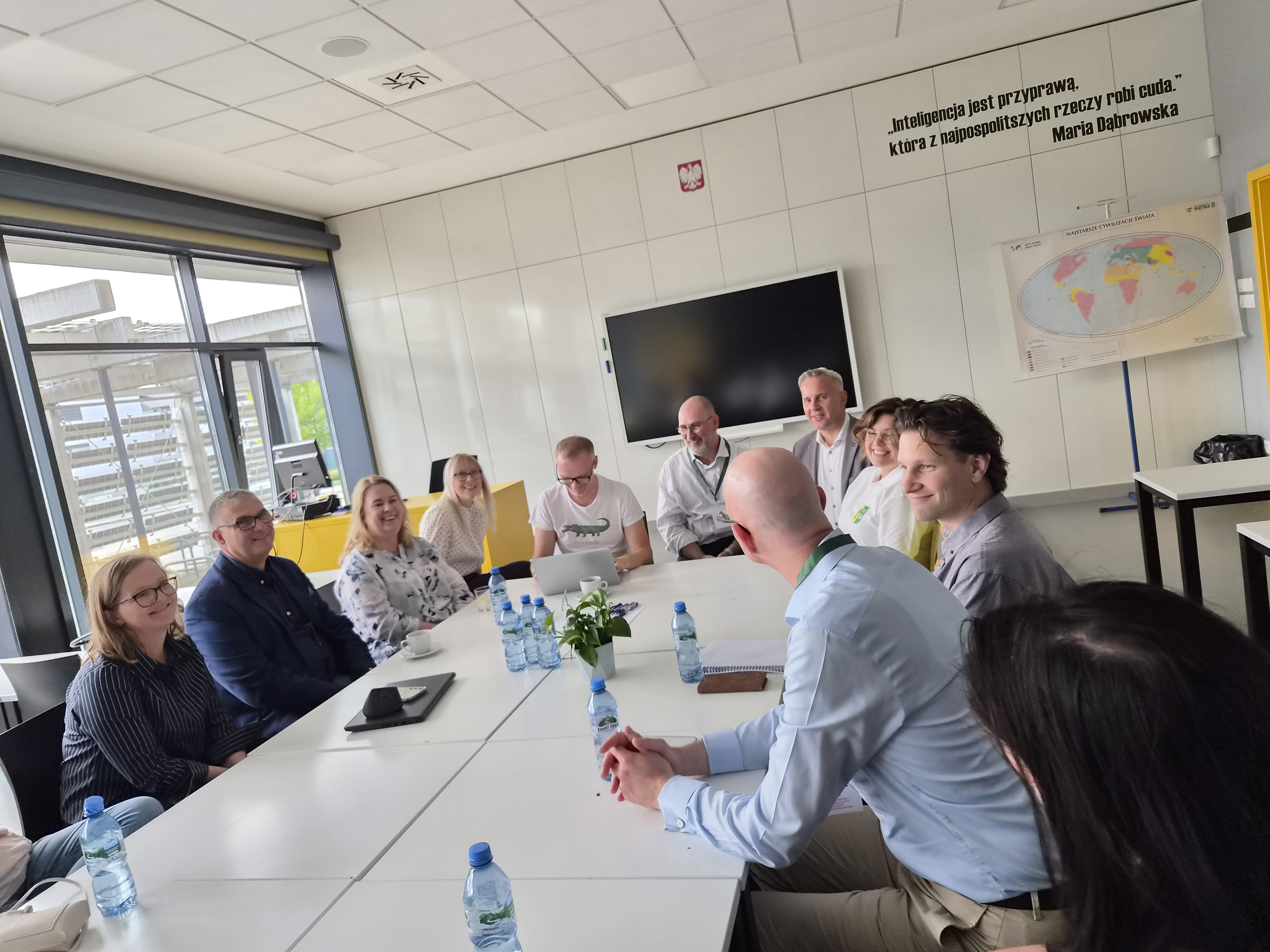 Zdjęcie: 10 os&oacute;b siedzących przy stole w&nbsp;szkolnej sali