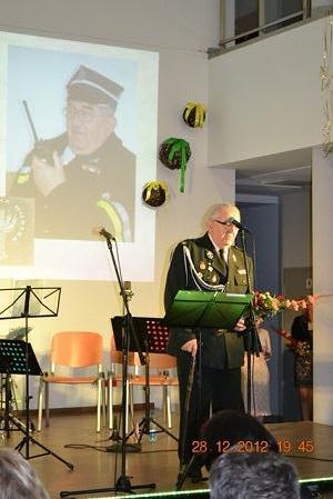 Na zdjęciu śp. Henryk Tarnowski w&nbsp;mundurze galowym strażackim. Stojący na&nbsp;scenie przy mikrofonie na&nbsp;statywie. Za nim duże zdjęcie z&nbsp;jego wizerunkiem wyświetlone na&nbsp;ekranie.