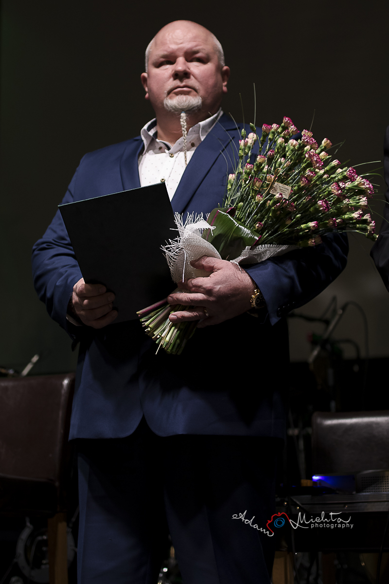 Karol Czerniak Na zdjęciu Karol Czerniak trzymający w rękach kwiaty, teczkę i statuetkę. Ubrany jest w granatowy garnitur i białą koszulę. Patrzy w dal.