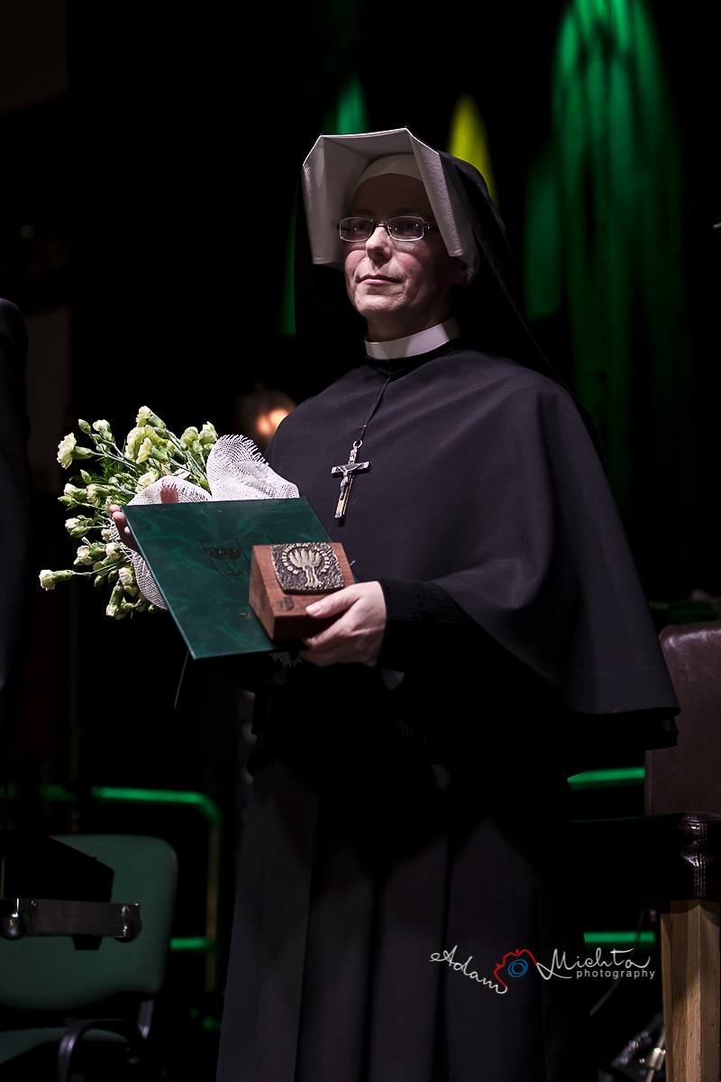 Zgromadzenie Sióstr Matki Bożej Miłosierdzia w Kiekrzu Na zdjęciu siostra zakonna w czarnym habicie z krzyżem na szyi. W rękach trzyma dyplom, statuetkę i bukiet kwiatów.