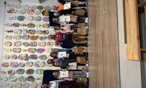 Dzieci stojące w rzędzie na scenie, odbierające dyplomy i nagrody za udział w konkursie gminnym Mistrz Pięknego Pisma. Dzieci trzymają białe teczki z herbem gminy Rokietnica, w tle jajka wielkanocne, rollup Gmina Rokietnica.